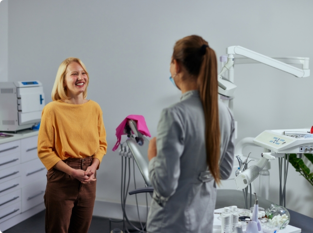 Young woman in yellow sweater talking to dental team member