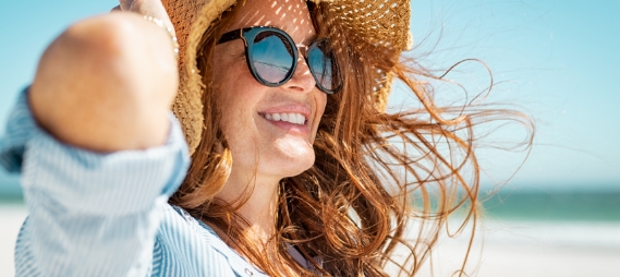 Smiling woman in sunhat and sunglasses sitting outdoors