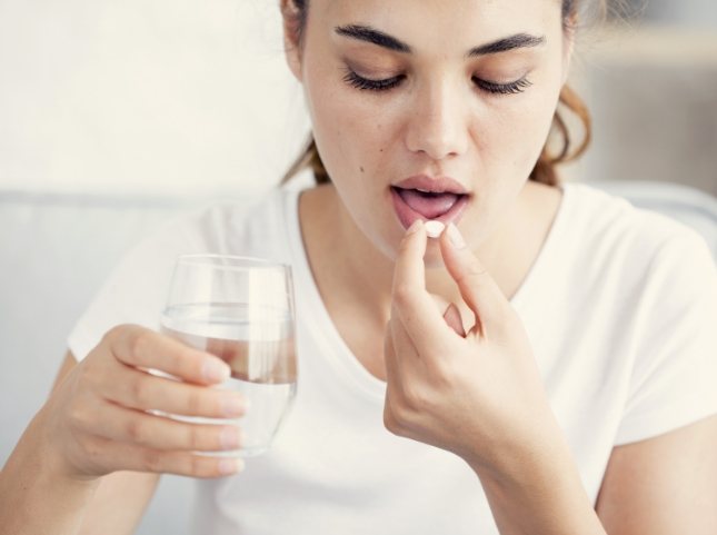 Woman taking white pill with glass of water