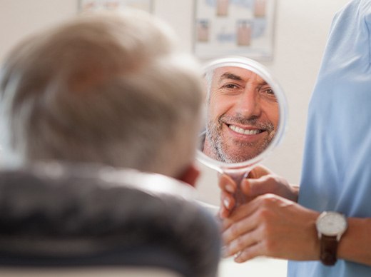 Man smiling while looking at reflection in handheld mirror