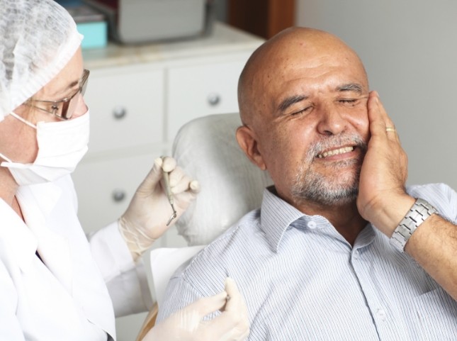 Man in dental chair wincing and touching his cheek