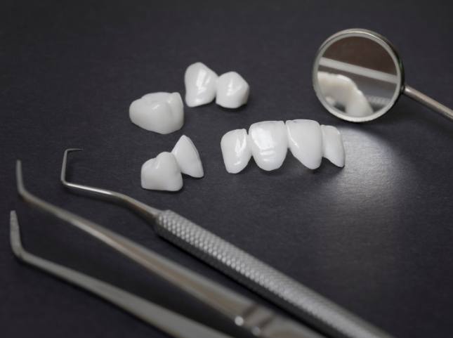 Several dental crowns and veneers on table next to dental mirrors