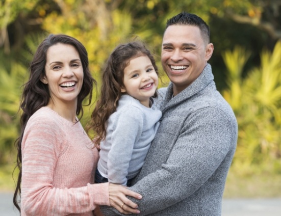 Mother and father smiling with their young daughter outdoors