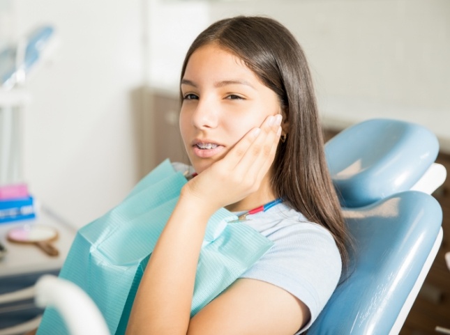 Teenage girl in dental chair wincing and touching her cheek