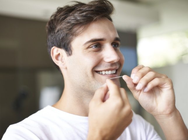 Man smiling and flossing his teeth