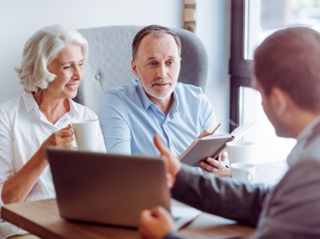 Man and woman talking to man with laptop across desk