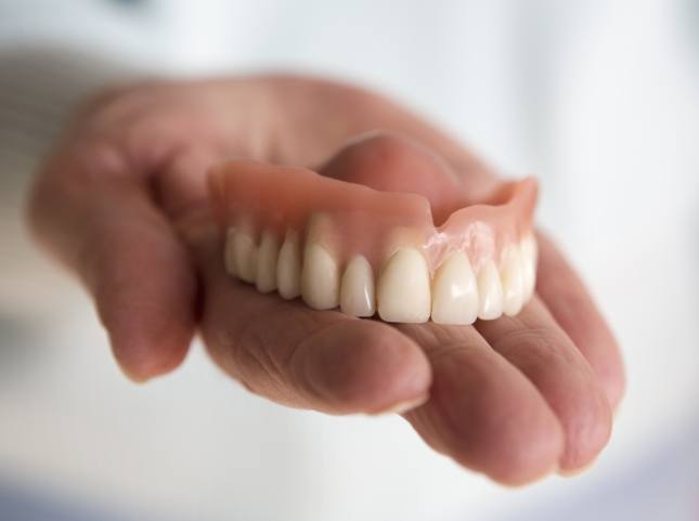 Hand holding a full upper denture