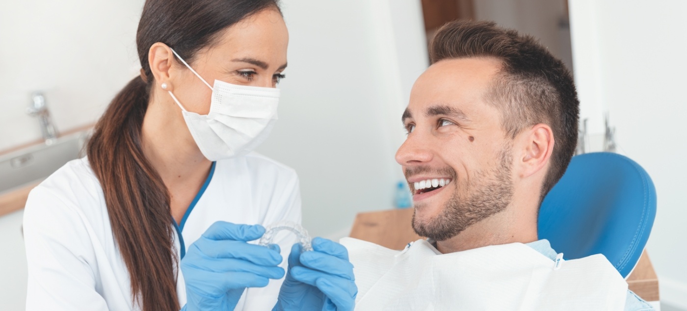 Man smiling at dentist holding Invisalign clear aligner