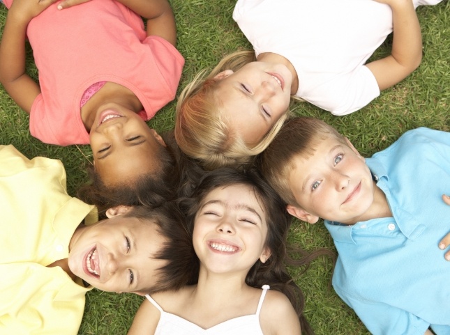 Circle of children laying in grass with their heads in the middle