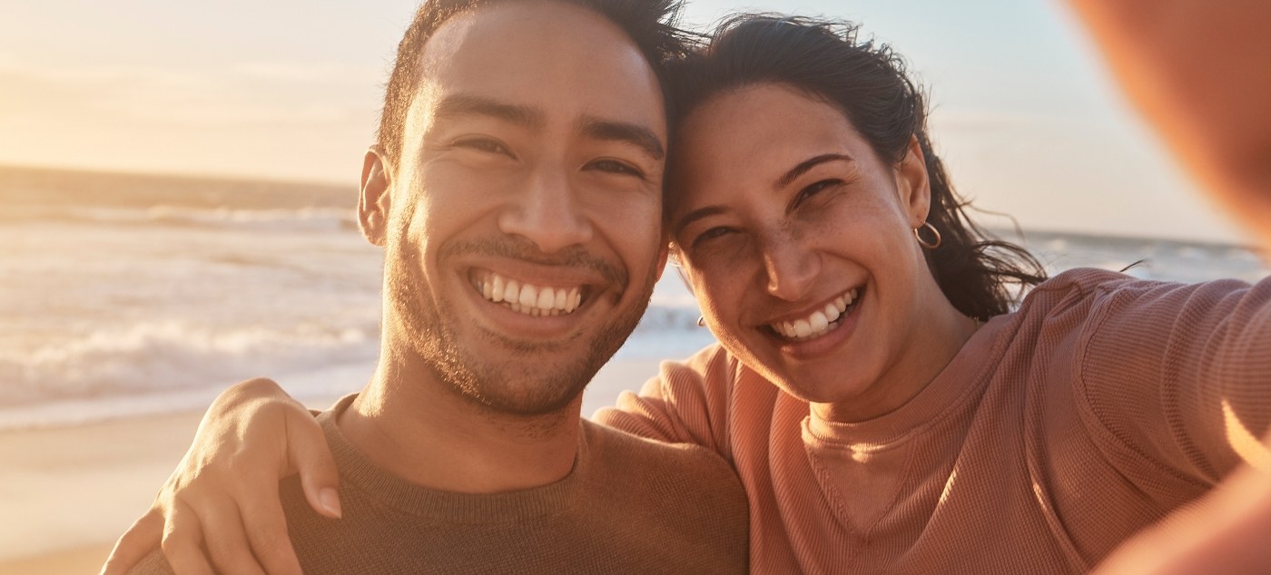 Man and woman taking selfie on beach after restorative dentistry in Newark
