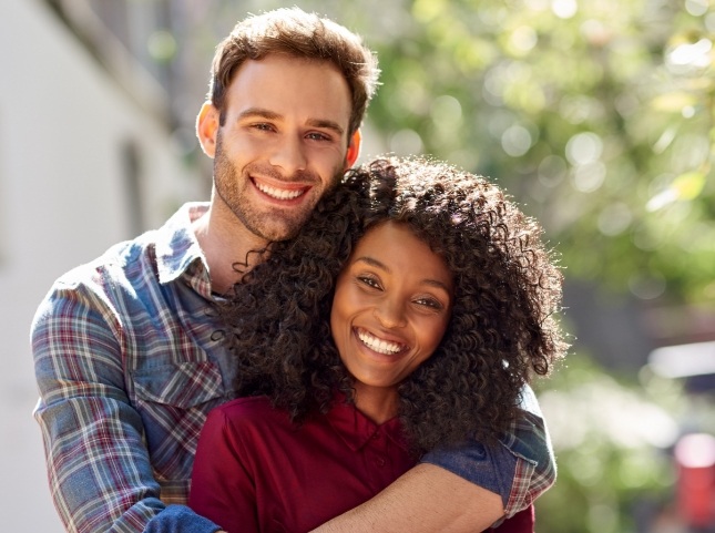 Man and woman hugging outdoors on sunny day