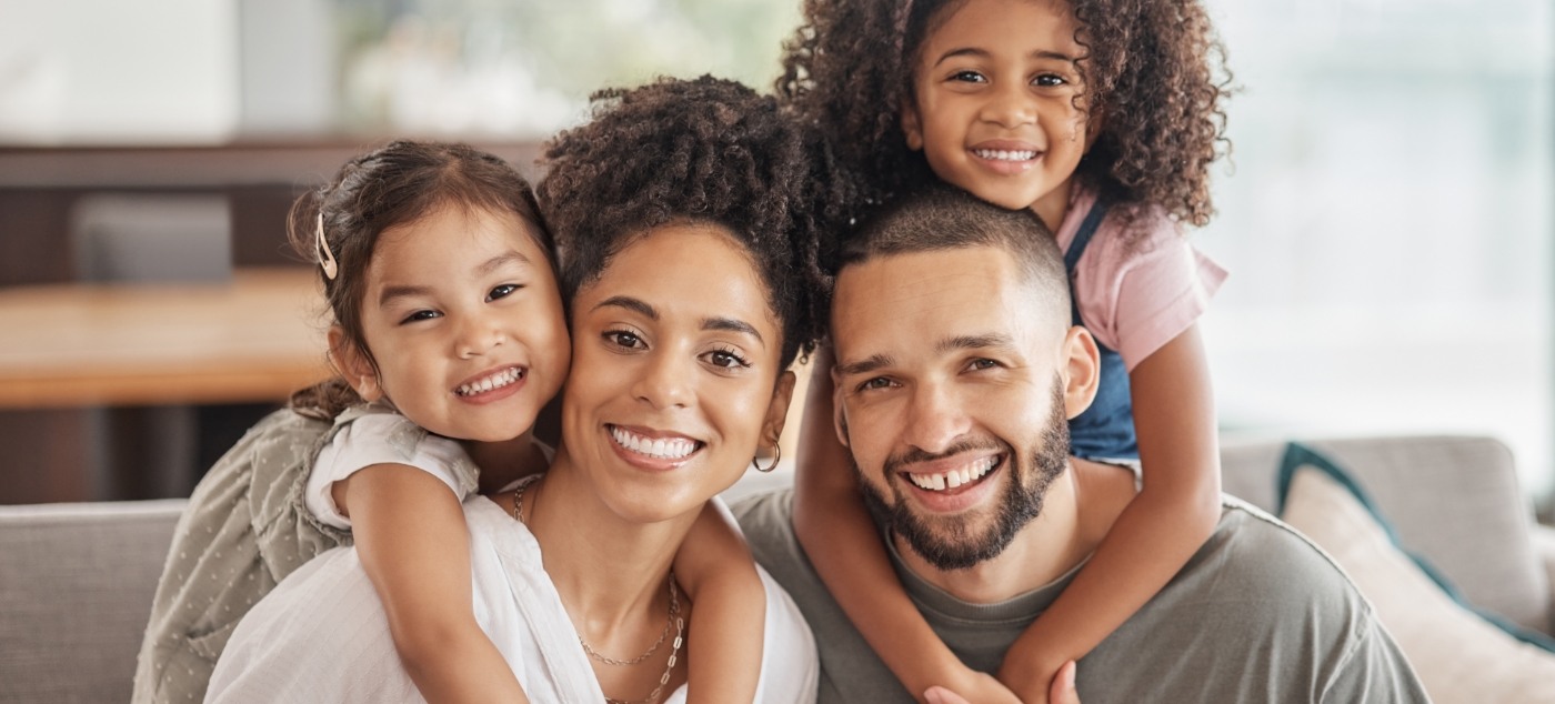 Family of four smiling on couch after root canal treatment in Newark