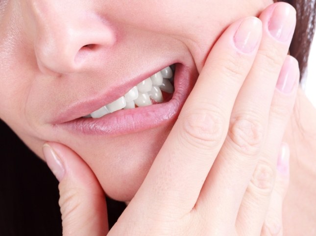 Close up of person wincing and touching their cheek before tooth extractions